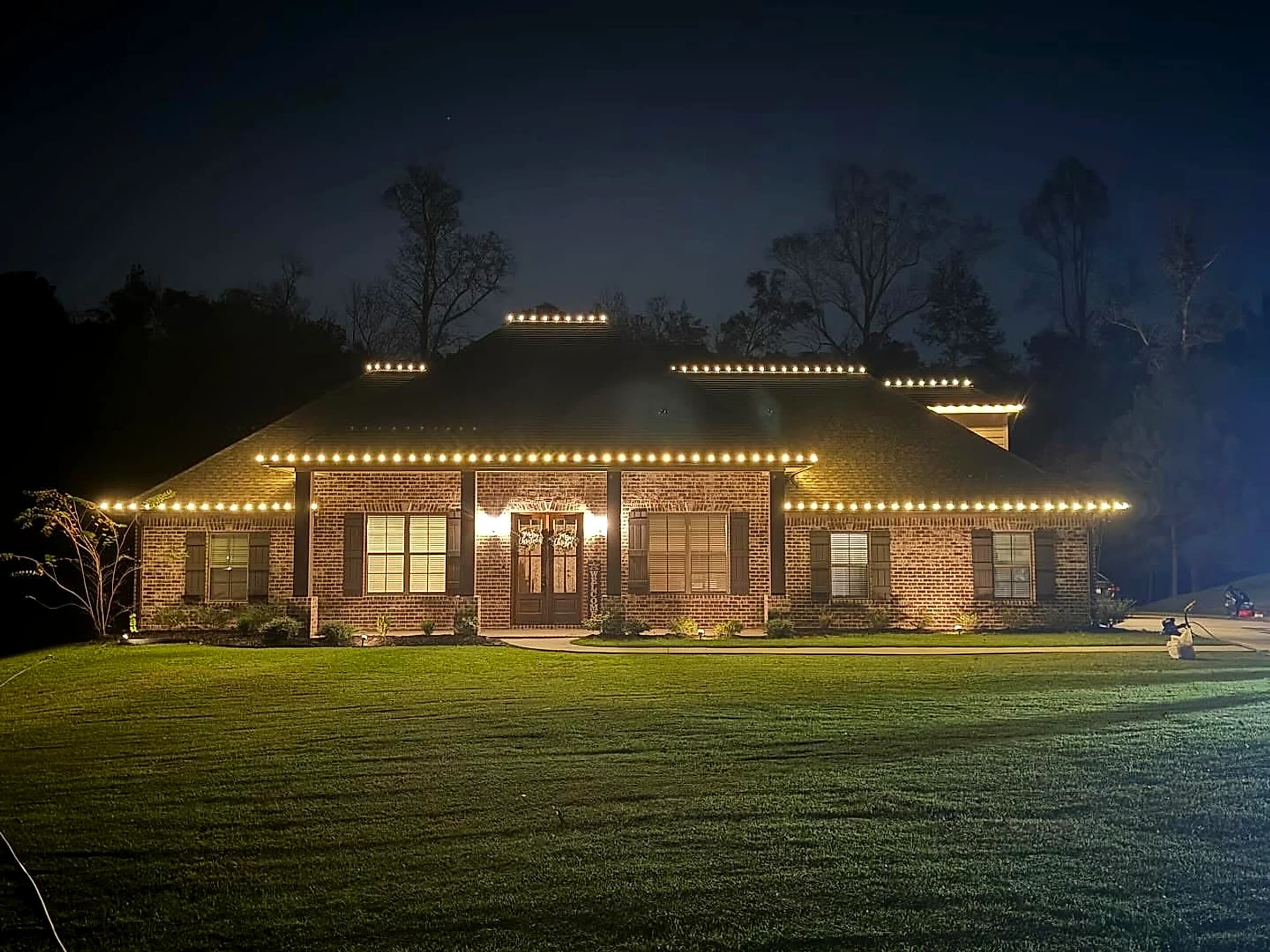 Southeast Lights display in Hattiesburg: a wide single-story brick home seen across a deep front lawn, warm white C9 along the eaves and along every ridge of the hip roof