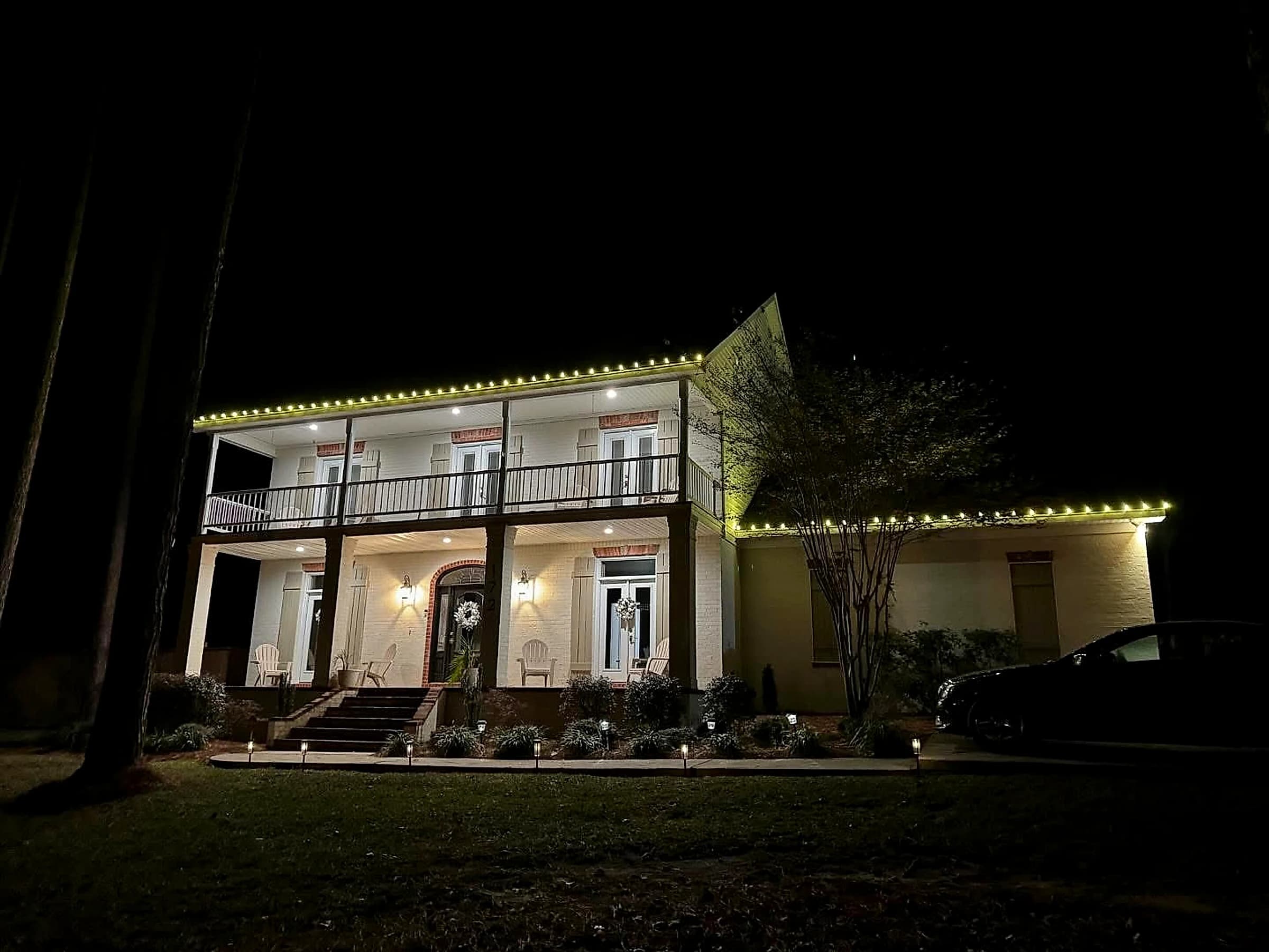 Southeast Lights display in Hattiesburg: a two-story house with double galleries at night, warm white C9 running along the front roofline twenty feet up and continuing along the lower wing roof