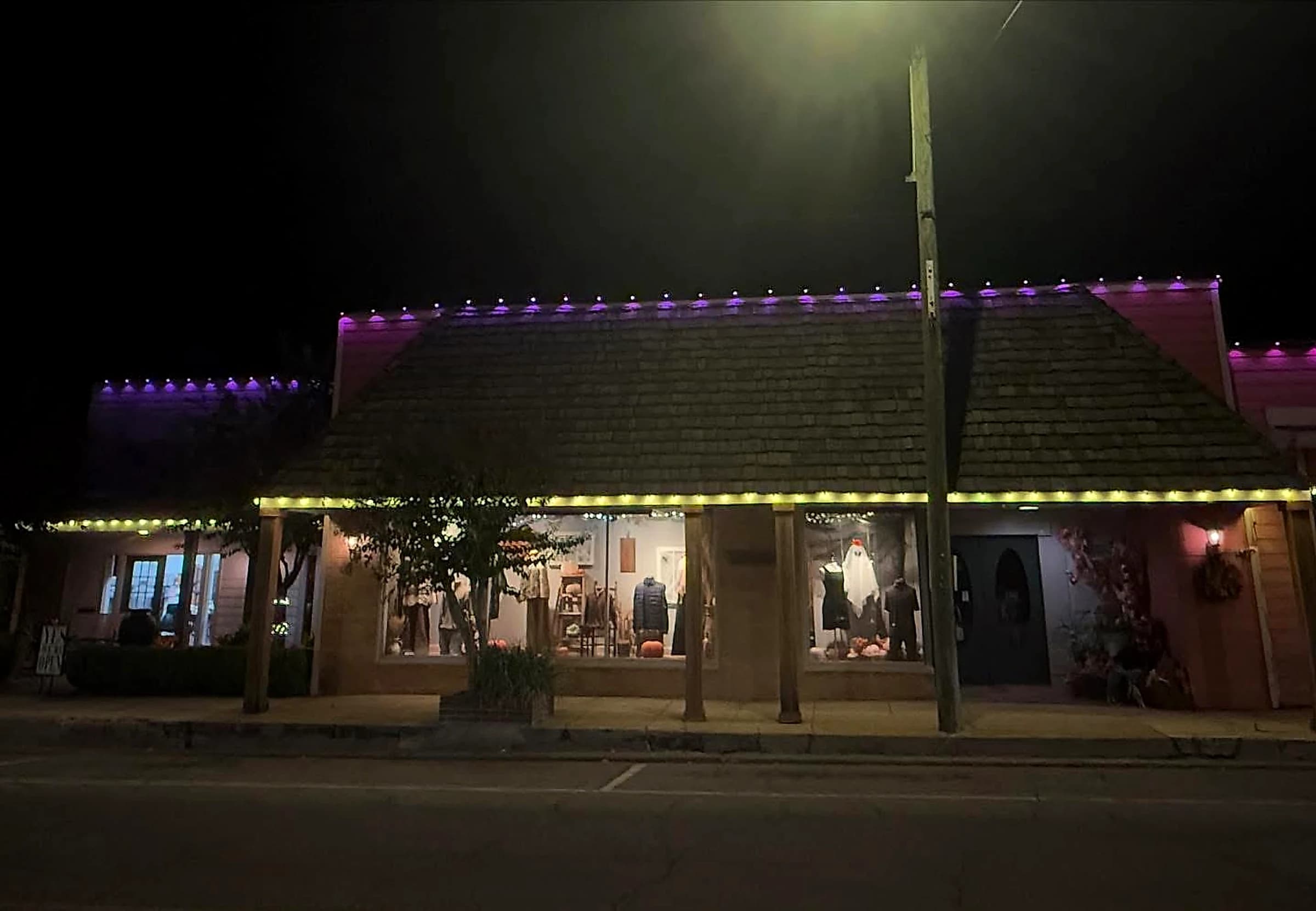 Southeast Lights display in Poplarville: the Apples Ltd. storefront at night with purple C9 bulbs along the upper roofline and warm white C9 along the porch fascia below, lit shop windows between them