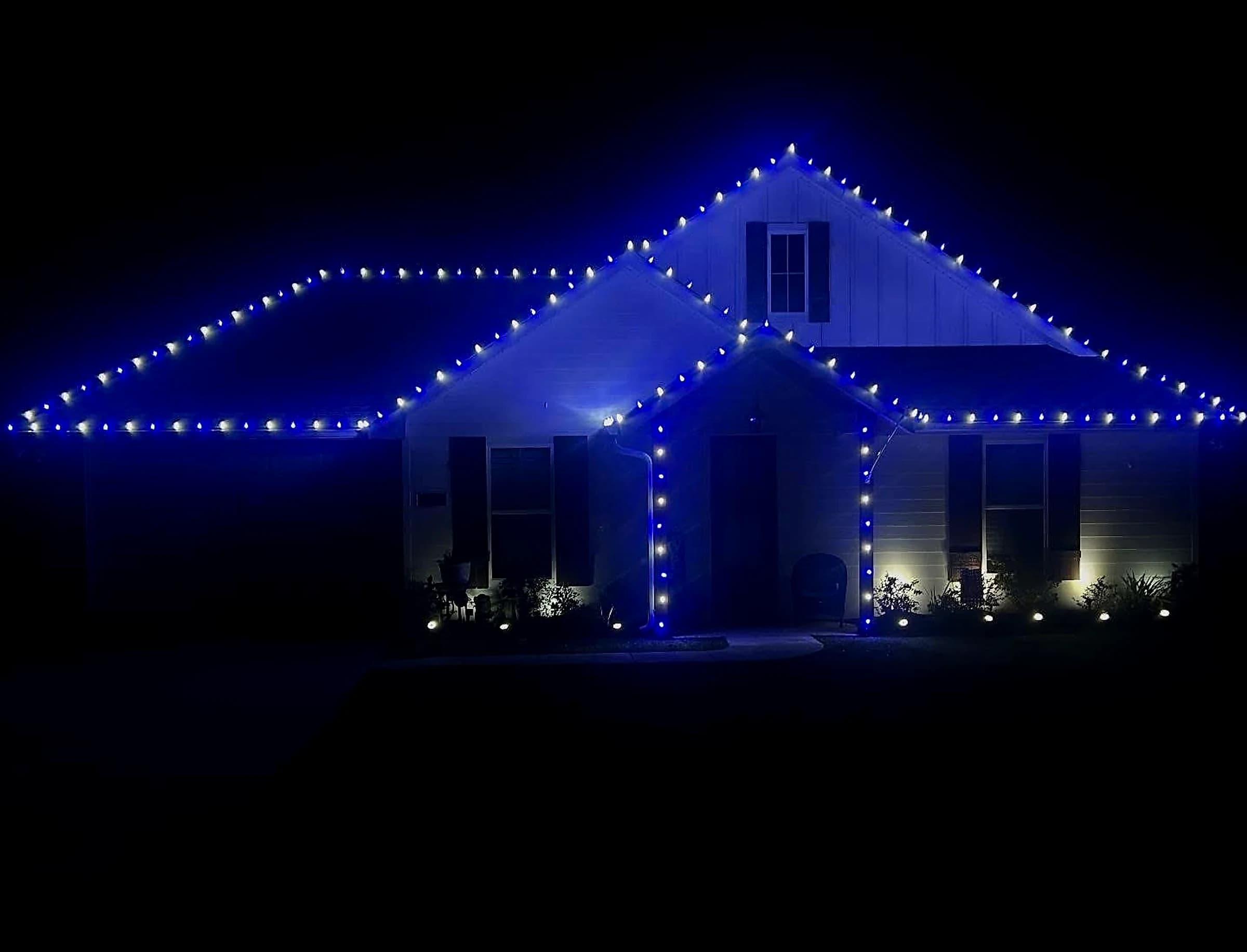 Southeast Lights display in Poplarville: a white craftsman home at night with alternating blue and bright white C9 bulbs along the roofline, gables and hips, and the porch columns wrapped in the same pattern