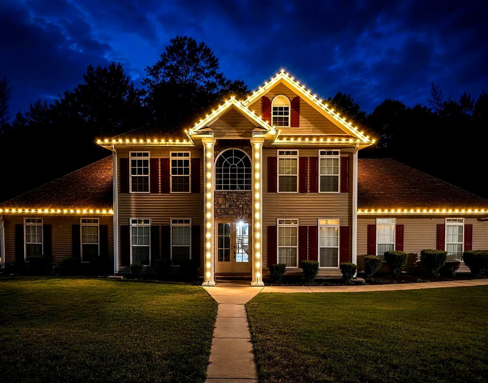 Southeast Lights display in Poplarville: a two-story colonial at dusk with warm white C9 along the main roofline, both wings and the center gable, and twenty-foot entry columns wrapped from base to capital