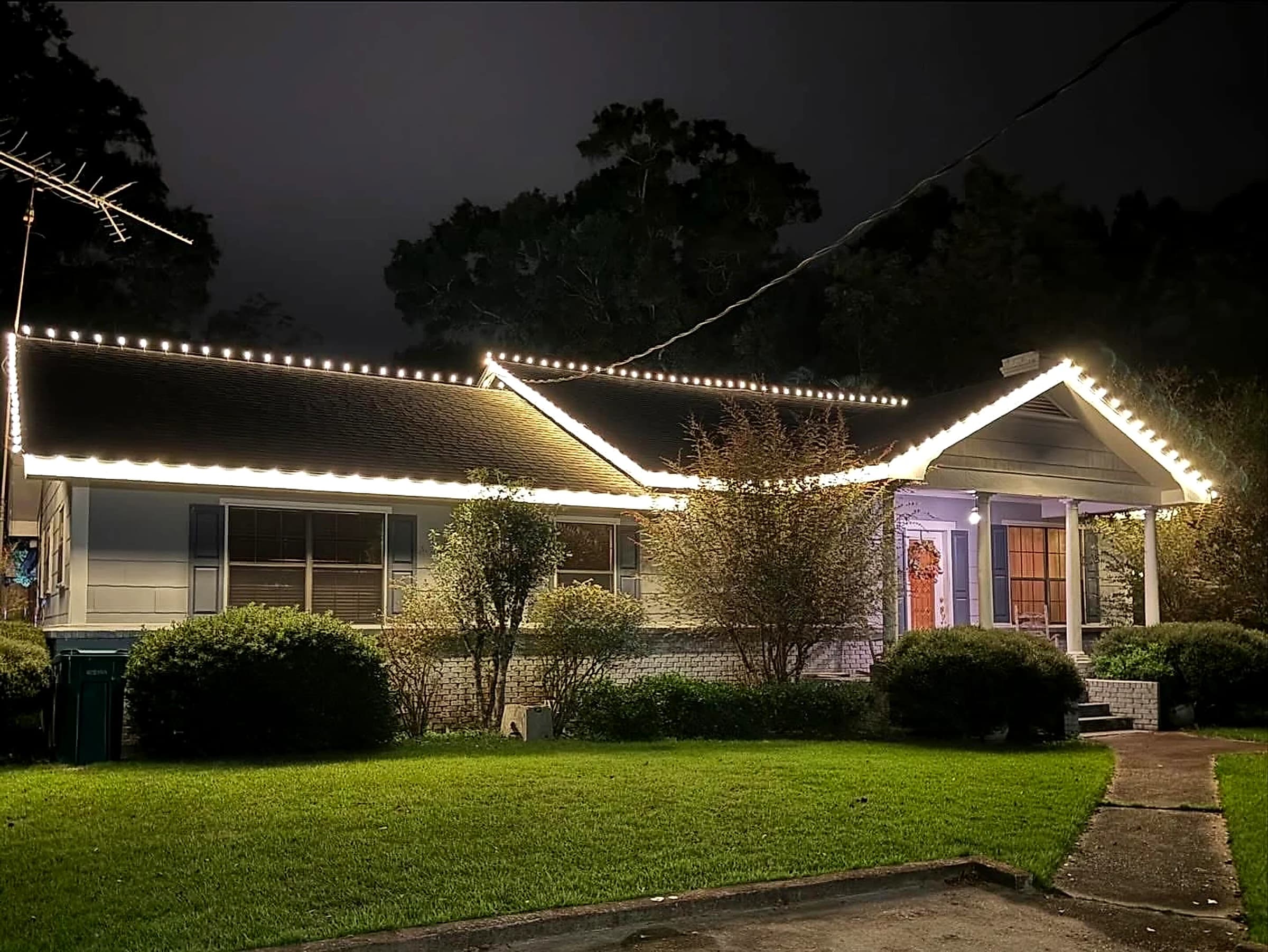 Southeast Lights display in Poplarville: warm white C9 running unbroken along the main eave, up over the porch gable rake and on past the far corner of the house