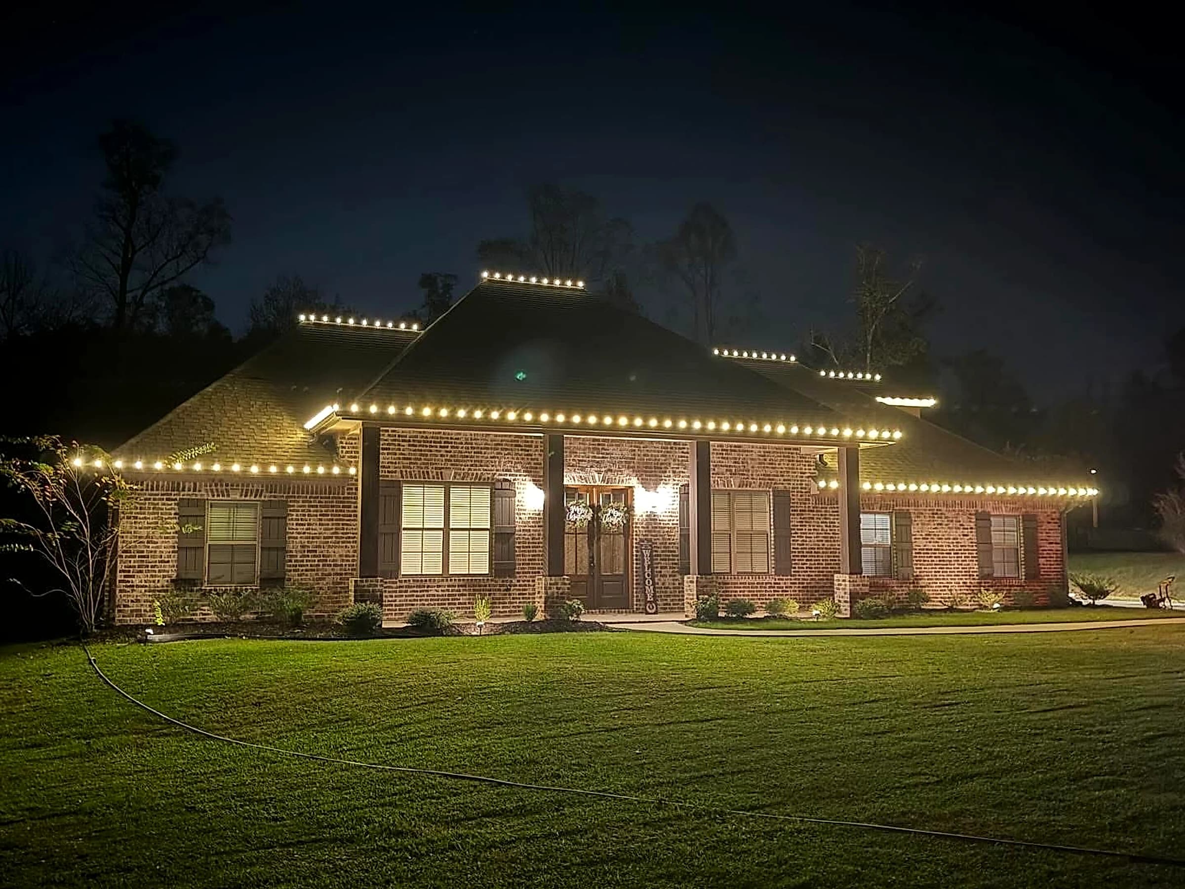 The same Hattiesburg house from the drive, warm white C9 picking out the eave line and the stepped ridges of the hip roof